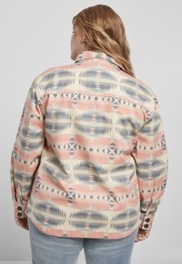 Langærmet mønstret skjorte med geometriske designs i rosa, blå og cremefarvede nuancer. Knapper ved ærmerne og en struktureret krave er synlige.