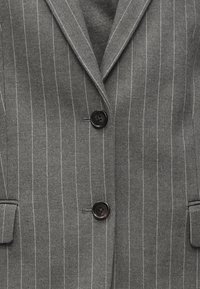Blazer gris a rayas con textura, que presenta solapas de muesca, dos bolsillos frontales y botones negros.