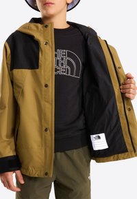 Brun og sort vandtæt jakke med hætte, der har lynlåslukning, lommer med knapklap og sort inderfor.