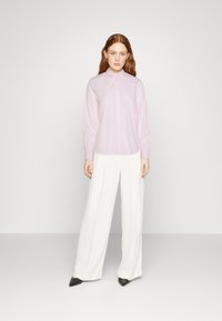 Camicia a righe rosa chiaro con bottoni e maniche lunghe, abbinata a pantaloni bianchi a gamba larga e scarpe nere a punta. Design semplice e strutturato.