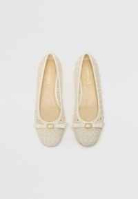 Bailarinas beige con un diseño trenzado, punta redondeada y una correa decorativa que cuenta con una pequeña hebilla dorada en la parte delantera.