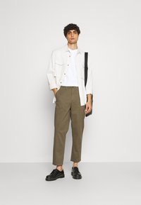 Camisa blanca de botones sobre una camiseta blanca, pantalones verde oliva y zapatos negros. Los pantalones tienen un corte recto y bolsillos laterales.