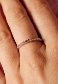 Silberner Ring mit einem glatten Band, das eine Reihe kleiner, klarer Steine entlang der Oberseite aufweist. Positioniert auf einer Hand mit strukturiertem Hautbild.