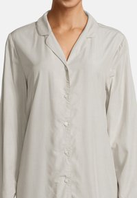 Camicia da pigiama grigia chiara in un tessuto morbido, con colletto, pattina dei bottoni e maniche lunghe. Design semplice e classico.