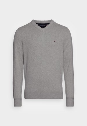 Jasnoszary sweter z długim rękawem i dekoltem w serek z małym haftowanym logo Tommy Hilfiger po lewej stronie klatki piersiowej.