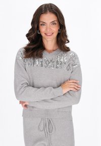 Maglione grigio con scollo a V, caratterizzato da un motivo decorativo di paillettes sul petto, texture morbida e polsini e orlo a coste.