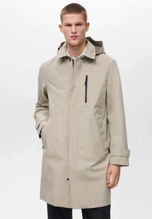 Beige vandtæt jakke med hætte, der har lynlåslomme på brystet, sidelommer og lige snit. Glat tekstur og minimalistisk design.