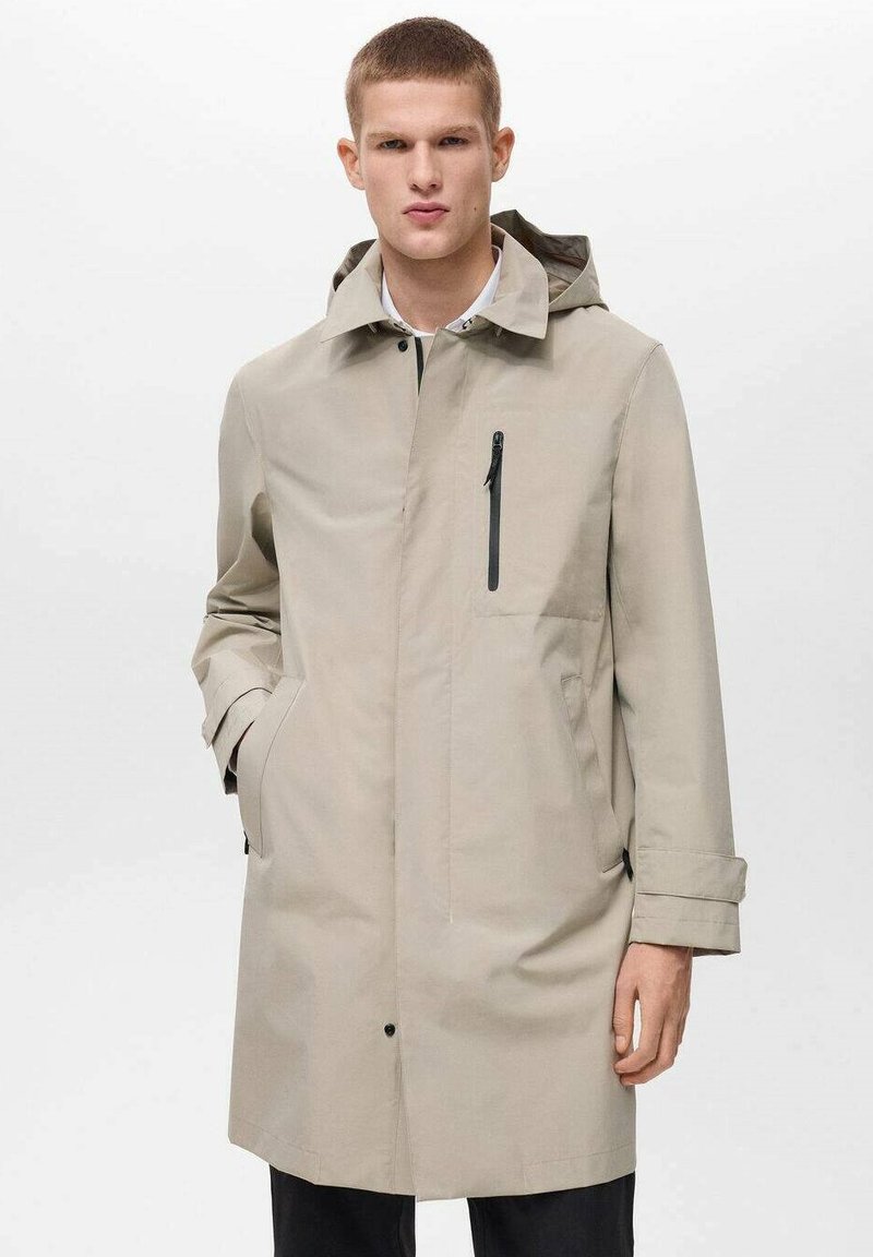 Cappotto impermeabile beige con cappuccio, dotato di tasca sul petto con zip, tasche laterali e taglio dritto. Texture liscia e design minimal.