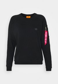 Sudadera negra hecha de una tela suave con un cuello redondo y mangas raglán. Cuenta con un bolsillo con cremallera y una etiqueta roja con texto en la manga.
