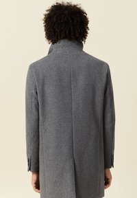Abrigo de lana gris con cuello alto, ajuste entallado y puños de un solo botón. La textura suave y las líneas limpias enfatizan un diseño moderno.