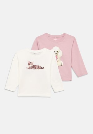 Duas camisetas de manga longa para crianças, uma branca com uma estampa de gatinho relaxando e outra rosa clara com uma estampa de poodle sentado.