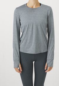 Harmaa pitkähihaurheilupaita, jossa on pyöreä pääntie ja peukalonreiät, yhdistetty tummiin kuvioituihin legginsseihin, valmistettu joustavasta, kosteutta siirtävästä materiaalista.