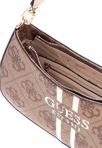 Borsa hobo in tessuto marrone a fantasia con strisce bianche e applicazioni in oro. L'interno presenta più scomparti e tasche con zip.