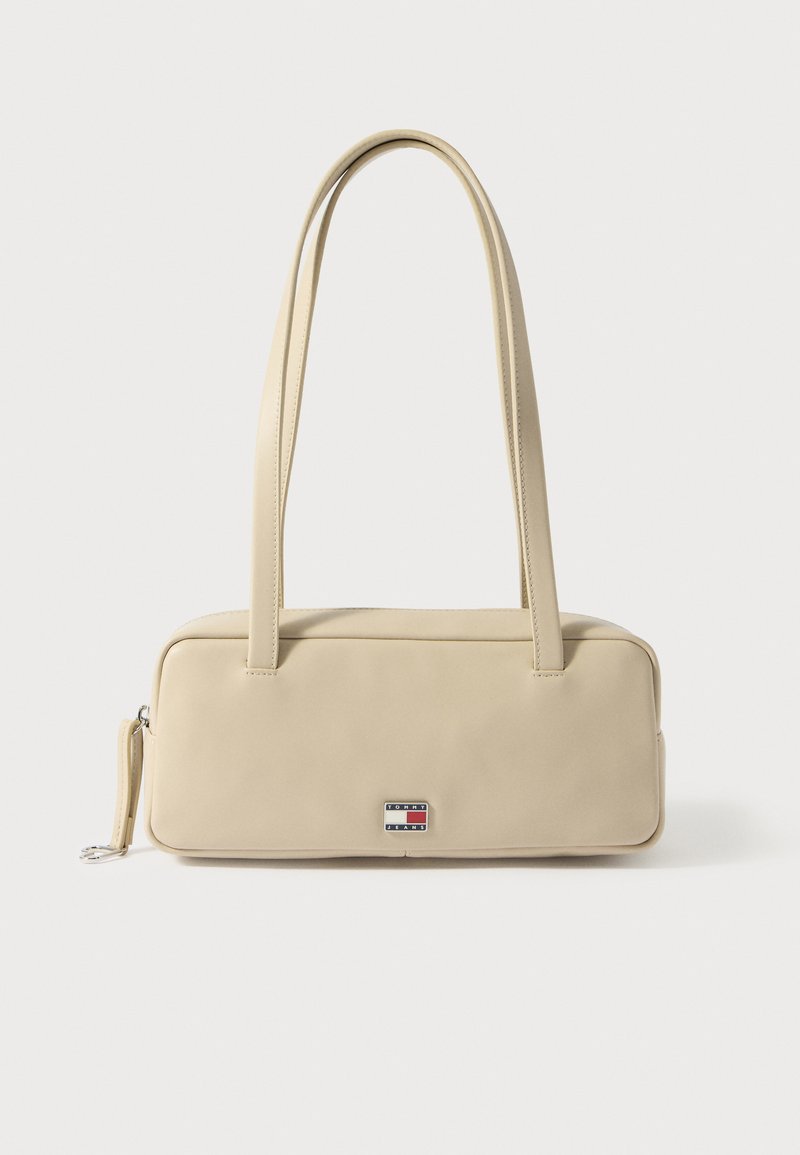 Μπεζ ορθογώνια τσάντα χειρός από λείο υλικό με δύο λαβές, κλείσιμο με φερμουάρ και μεταλλικό λογότυπο μάρκας στο μπροστινό μέρος.