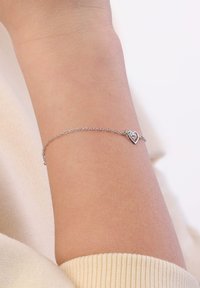 Zilveren kettingarmband met een hartvormige charme met een heldere edelsteen in het midden. De ketting is delicaat en fijn verbonden.