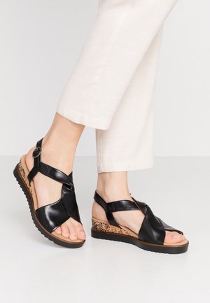 Mustat nahkaiset wedge-sandaalit, joissa on ristikkäinen muotoilu, teksturoitu korkkikorko ja kumipohja. Säädettävä hihna turvallista istuvuutta varten. Litteät, avoimet varpaat.