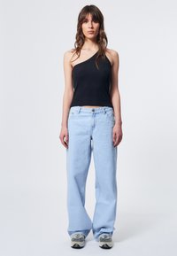 Schwarzes geripptes Top mit einem Schulterträger, hellblaue lässige Jeans, graue Sneaker, stehend vor einem schlichten Hintergrund.