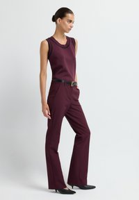 Haut sans manches bordeaux avec des bordures noires, associé à un pantalon bordeaux ajusté. Une ceinture noire et des escarpins noirs à bout pointu complètent le look.
