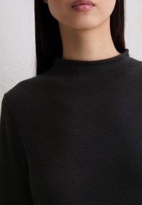 Schwarzer Pullover mit hohem Kragen aus weichem Strickstoff, mit minimalistischem Design, langen Ärmeln und glatter Textur.