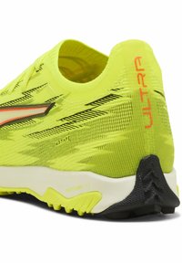 Lys gul løbesko med sorte detaljer og tekstureret overdel. Har en polstret sål og tydelig "ULTRA" branding på hælen.