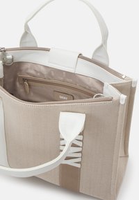 Sac en toile beige avec des accents en cuir blanc, doté d'une fermeture éclair, de poches intérieures et d'un logo DKNY embossé sur la doublure.
