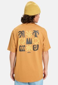 Kortærmet, sennepsfarvet t-shirt med abstrakte sorte og gule mønstre på bagsiden, lavet af blødt bomuldsstof.