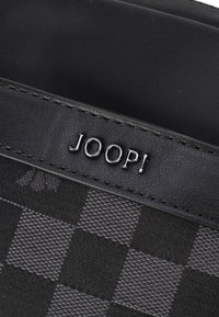 Črna denarnica iz karo tkanine z gladkimi usnjenimi poudarki. Ponaša se z vtisnjenim logotipom "JOOP!" v srebrni barvi in teksturiranim šivom.