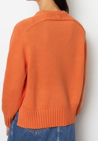 Maglione arancione lavorato a maglia con orlo e polsini a costine, caratterizzato da un collo rotondo e tessuto testurizzato. La vista posteriore mostra i dettagli delle spalle.
