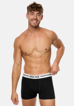 Boxers en coton noir avec une ceinture blanche portant l'inscription "INDICODE" et des accents rayés. Le design est ajusté avec une texture lisse.