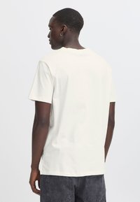Camiseta de algodón blanca con mangas cortas, cuello redondo y corte relajado. Presenta una textura suave y un diseño minimalista sin gráficos.