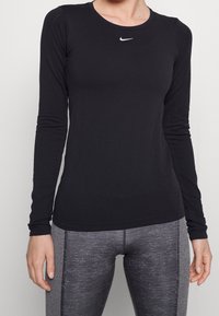 Maglietta atletica nera a maniche lunghe con scollo rotondo, tessuto strutturato e un piccolo logo Nike bianco sul petto.
