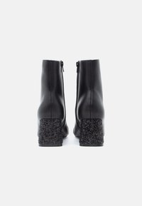 Μαύρες αστράγαλες μπότες με κομψό δερμάτινο άνω μέρος και υφή μαύρης γυαλιστερής γόβας. Διαθέτουν πλαϊνούς φερμουάρ για εύκολη χρήση.