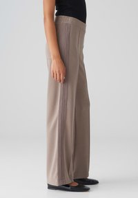 Brede broek in lichtbeige, uitgerust met een elastische tailleband en verticale ribbelaccenten aan de zijkanten. Gemaakt van zachte stof.