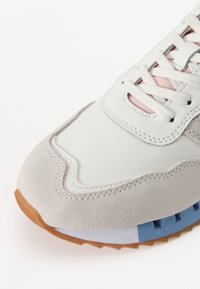 Heled hallid ja beeži suede'ist sneakers valge võrgust ülemise osaga, millel on sinine ja pruun tekstuuriga kummikreen. Paelad on heledat roosat värvi.