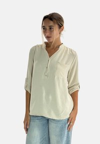 Blusa de manga larga en beige claro con escote henley abotonado, bolsillo en el pecho y puños enrollados; tejido texturizado con un ajuste relajado.