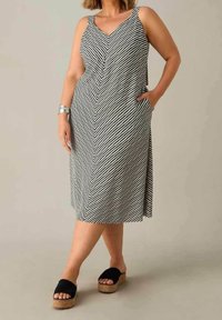 Černo-bílá pruhovaná midi šaty s V-výstřihem, širokými ramínky a kapsami; doplněné černými platformovými sandály. Hladká textilie.