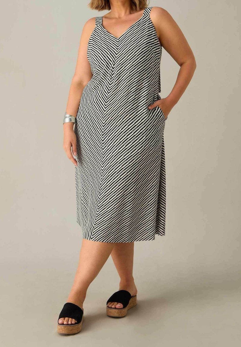 Černo-bílá pruhovaná midi šaty s V-výstřihem, širokými ramínky a kapsami; doplněné černými platformovými sandály. Hladká textilie.