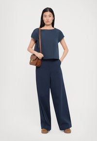 Top scurt de culoare albastru marin, asortat cu pantaloni largi de culoare albastru marin, geantă de umăr maro și pantofi cu platformă maro. Design simplu și culori uni.