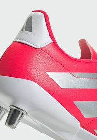 Scarpino da calcio rosa brillante con tomaia in pelle testurizzata, rifiniture argentate e un contrafforte bianco con finitura liscia. Include tacchetti in metallo.