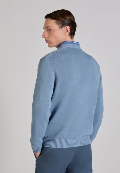 Light blue knit sweater with a high collar and ribbed cuffs and hem. Smooth texture enhances its casual design. Worn over dark trousers.