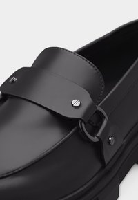 Μαύρο δερμάτινο μοκασίνι με φαρδιά λωρίδα και ασημένιες λεπτομέρειες στο επάνω μέρος, με χοντρή σόλα και λείο φινίρισμα.