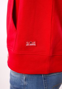 Sweat-shirt rouge en tissu texturé avec ourlet côtelé, orné d'un patch logo rectangulaire rouge et bleu Lee Cooper sur le bas devant.