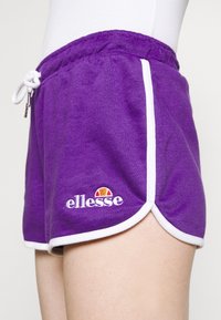Shorts en tricot violet avec accents blancs et taille élastique. Présentent un cordon blanc et un logo brodé en bas à gauche.