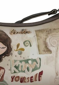 Schultertasche in Cremefarbe mit gestickten Motiven, darunter eine Frau und der Schriftzug "Know Yourself", mit metallischen Akzenten und einer strukturierten Oberfläche.