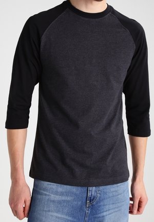 Sort og mørkegrå raglanærmeskjorte lavet af blødt stof, med trekvartærmer og rund halsudskæring, parret med lyse jeans.