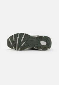 Semelle d'une basket avec une bande de roulement en caoutchouc noir et blanc, présentant des rainures et des motifs pour l'adhérence et la flexibilité sur un fond uni.