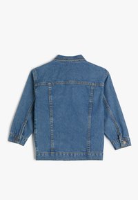 Chaqueta de mezclilla en azul medio, con un cuello clásico, mangas largas y puños abotonados. Costuras visibles y detalle en el yugo trasero.