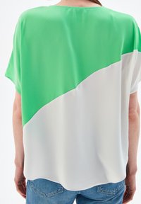 Haut à manches courtes vert et blanc présentant un design bicolore avec un tissu lisse et un ourlet arrondi, vu de dos.