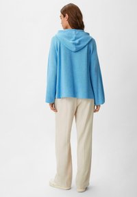Helles blaues Kapuzensweatshirt mit strukturiertem Strickdesign, langen Ärmeln und lockerer Passform, kombiniert mit off-weißen, weit geschnittenen Hosen.