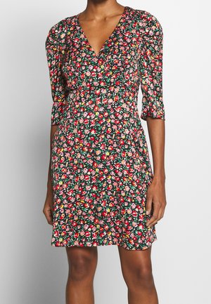 Kvinde iført en knælænge kjole med blomsterprint, V-hals og trekvart puffede ærmer mod en ensfarvet grå baggrund.